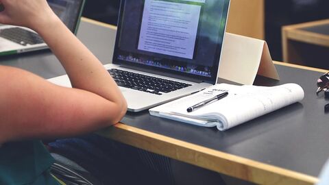 Person, von der nur ein Arm zu sehen ist, sitzt vor einem Laptop an einem Tisch.