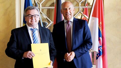 Michael Knab steht vor einer Wand mit Flaggen und hält seine Ernennungsurkunde in den Händen, neben ihm steht Prof. Dr. Roman Poseck.